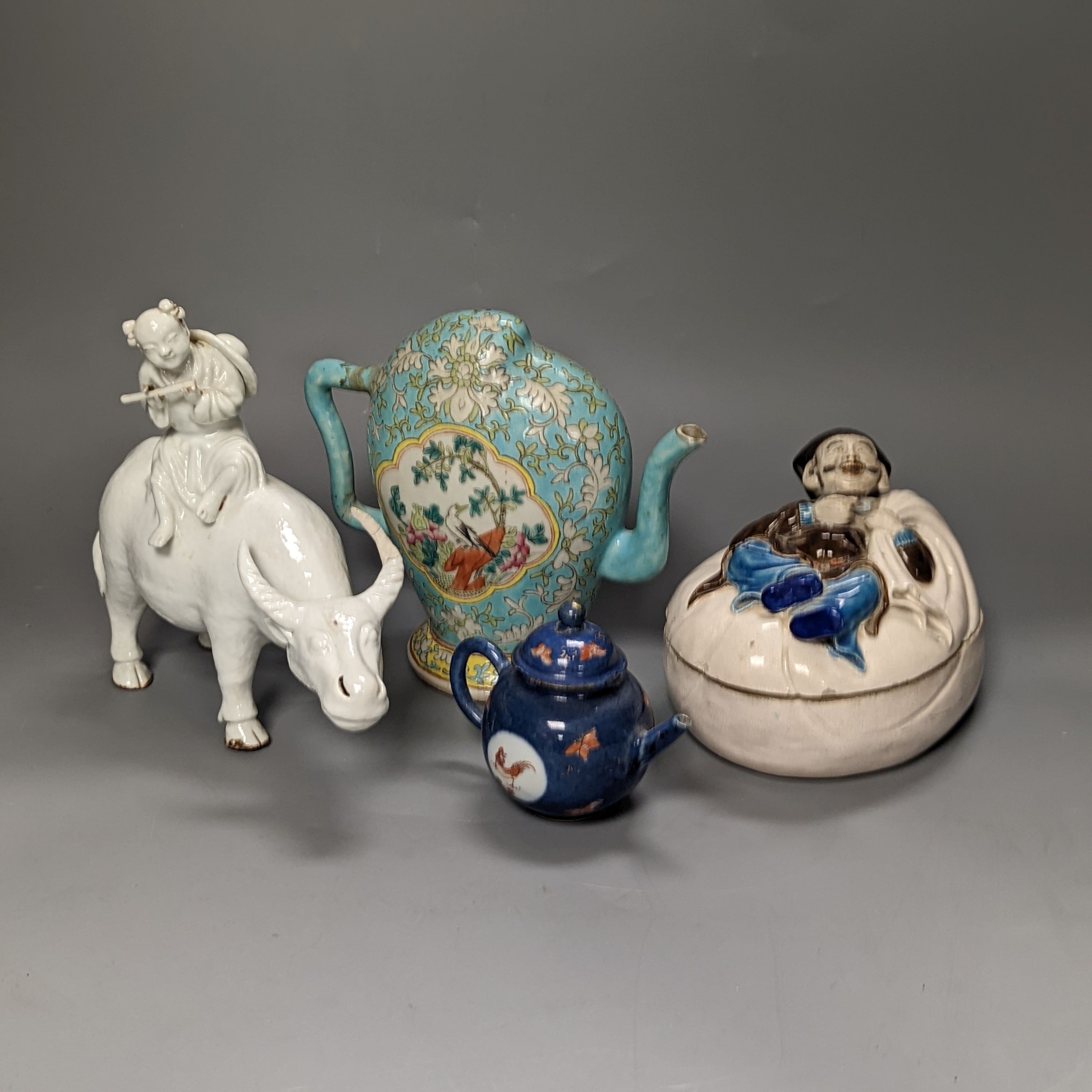 A 19th century Cadogan shape Chinese wine ewer, a Chinese blanc de chine figure riding an ox, an 18th century Chinese miniature blue ground ‘cockerel’ teapot and a Japanese Daikoku figural box and cover. Tallest 19cm